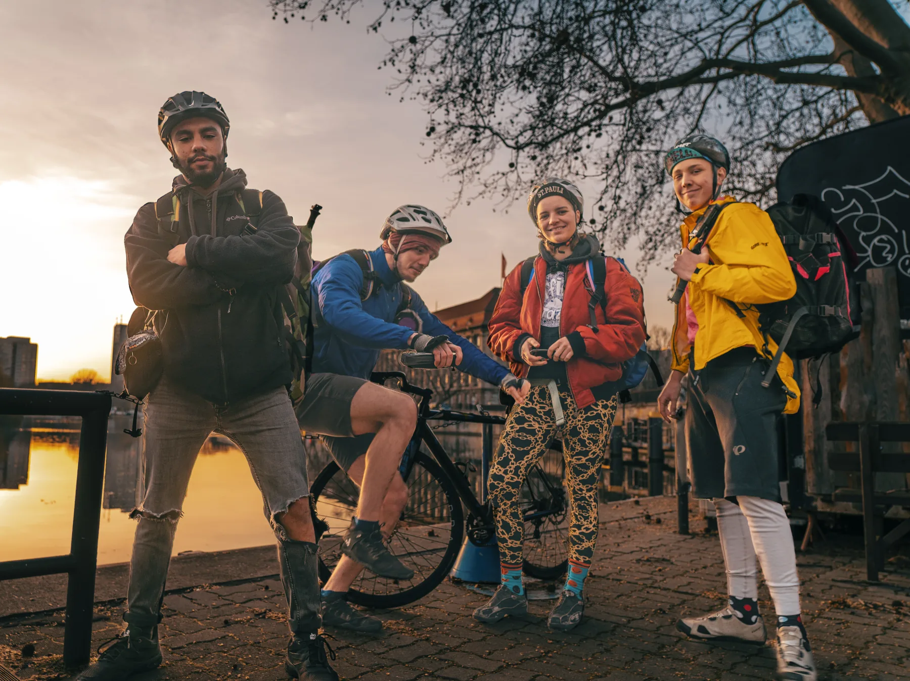 Four Khora couriers standing together with bicycles and delivery bags at sunset.