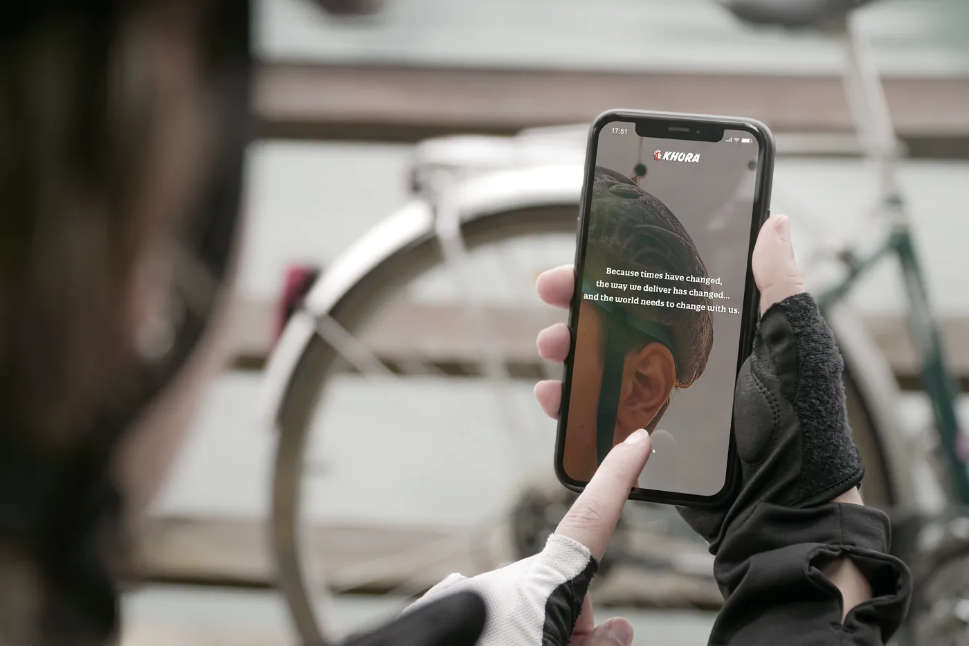 Person holding a phone with a Khora campaign message displayed over a courier photograph.